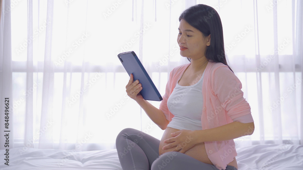 A portrait of happy Asian pregnant woman using, working online with computer laptop notebook tablet device with screen in bedroom at home. Having a baby. Family people lifestyle. Mom love. A portrait of happy Asian pregnant woman using, working online with computer laptop notebook tablet device with screen in bedroom at home. Having a baby. Family people lifestyle. Mom love.
