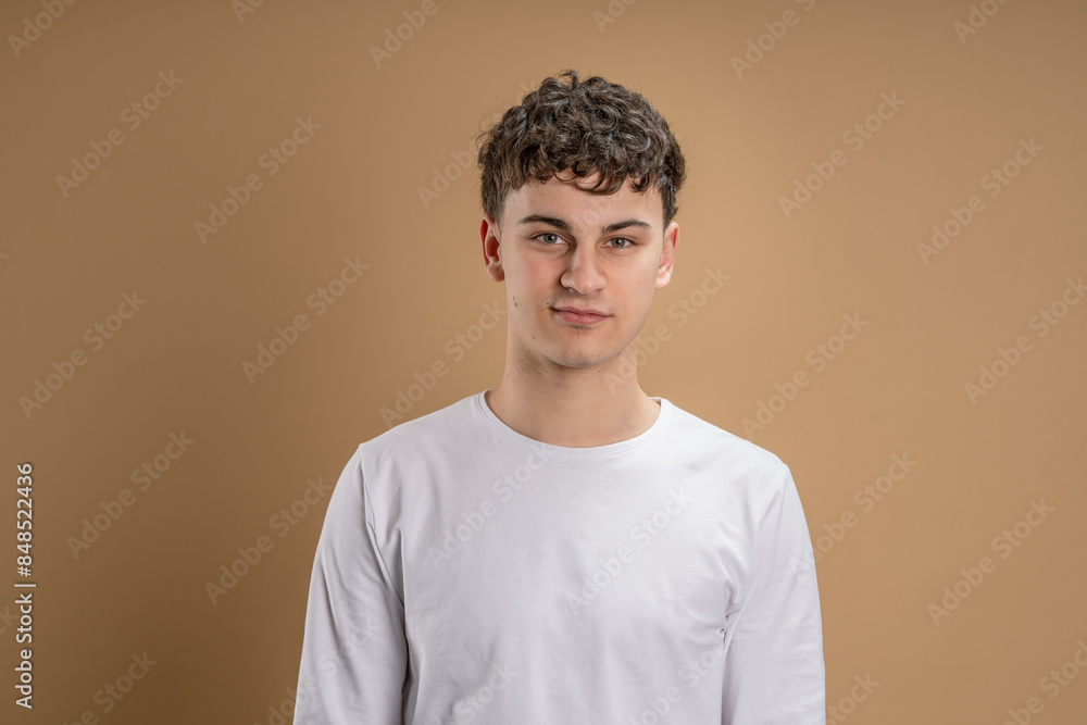 Portrait of one caucasian man 20 years old looking to the camera in front of almond color studio background wearing casual shirt copy space Portrait of one caucasian man 20 years old looking to the camera in front of almond color studio background wearing casual shirt copy space