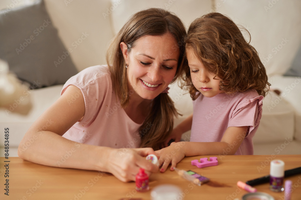 Young mother and little girl painting the nails while using makeup and playing together at home Young mother and little girl painting the nails while using makeup and playing together at home