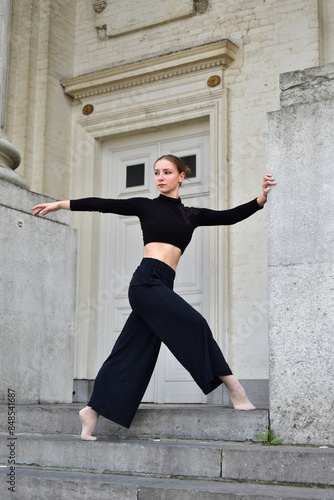 Young woman in black outfit performing a contemporary dance move on stone stairs photo