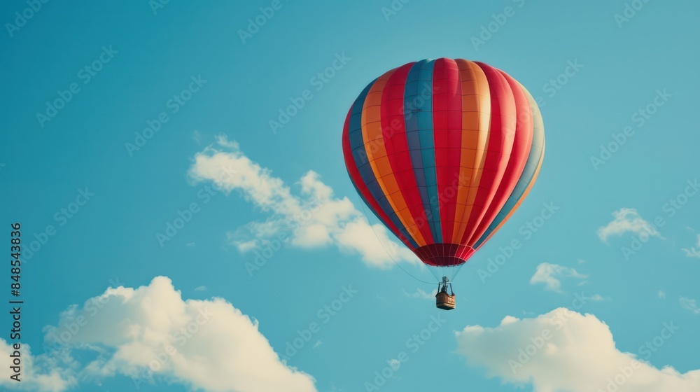 Obraz premium A vibrant hot air balloon floating amidst fluffy clouds against a crisp blue sky, symbolizing adventure and exploration