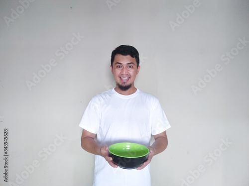 Adult Asian man showing excited expression while holding empty dinner plate photo