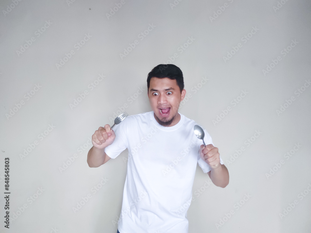 Excited Asian man holding spoon and fork in his hands Excited Asian man holding spoon and fork in his hands