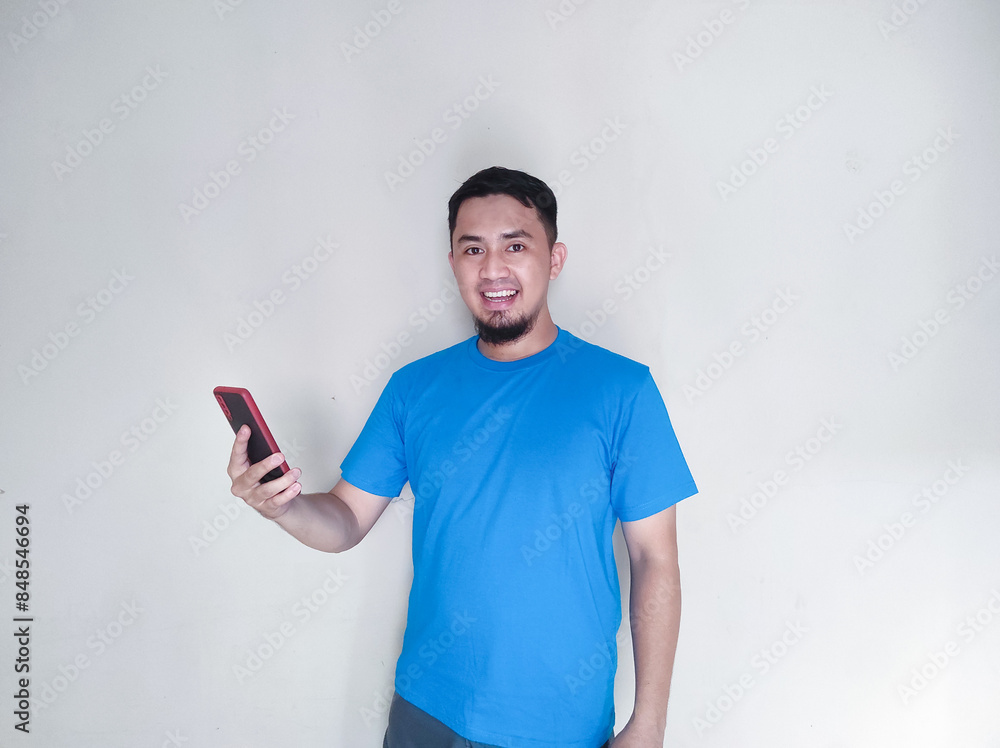 Adult Asian man smiling happy while holding a cellular phone Adult Asian man smiling happy while holding a cellular phone
