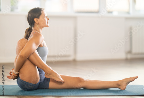 Sporty young girl maintaining active lifestyle training in cozy yoga studio, performing powerful dynamic asanas to improve body flexibility, balance and strengthen core