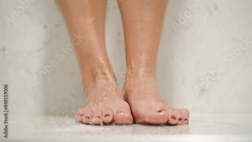 Naked Woman's Legs in the Shower with White Marble Walls, water droplets falling down.