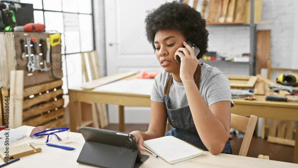 African american woman on phone in workshop using tablet for business African american woman on phone in workshop using tablet for business