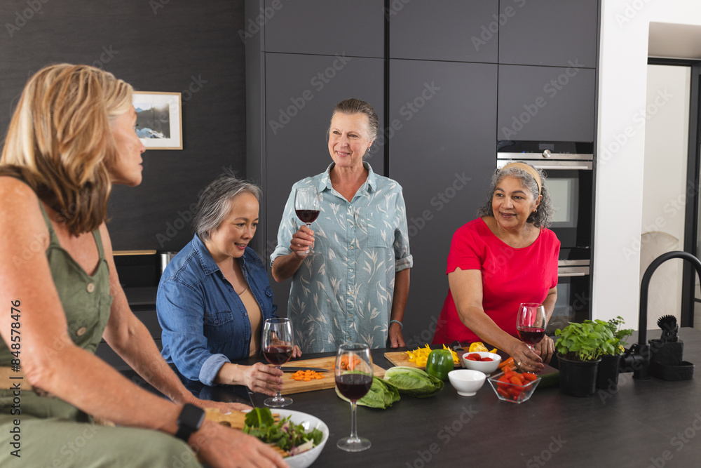 Diverse group of mature women enjoying wine and preparing food together in kitchen Diverse group of mature women enjoying wine and preparing food together in kitchen