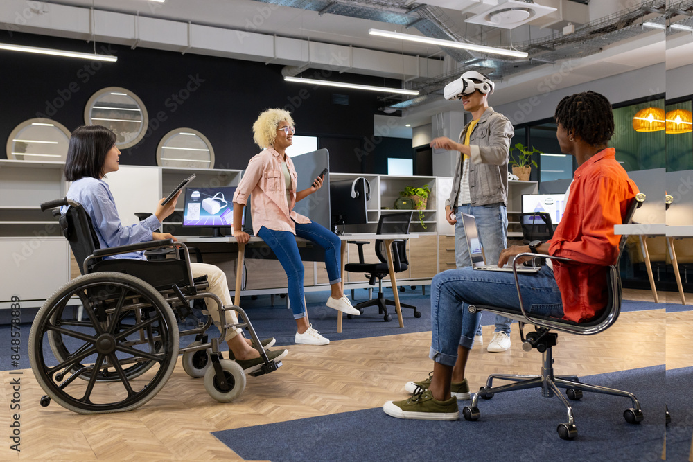 Obraz premium Business colleagues in office watching man using vr headset, asian woman in wheelchair, inclusivity