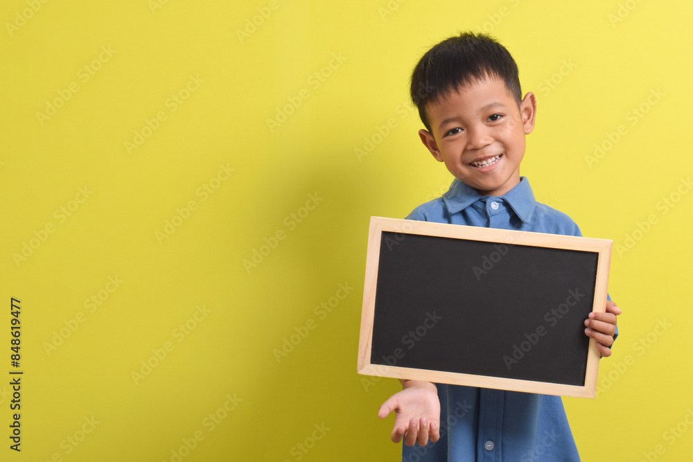 Cute little Asian boy holding a blank chalk board isolated on yellow background. Space for text, copy space, mockup banner Cute little Asian boy holding a blank chalk board isolated on yellow background. Space for text, copy space, mockup banner