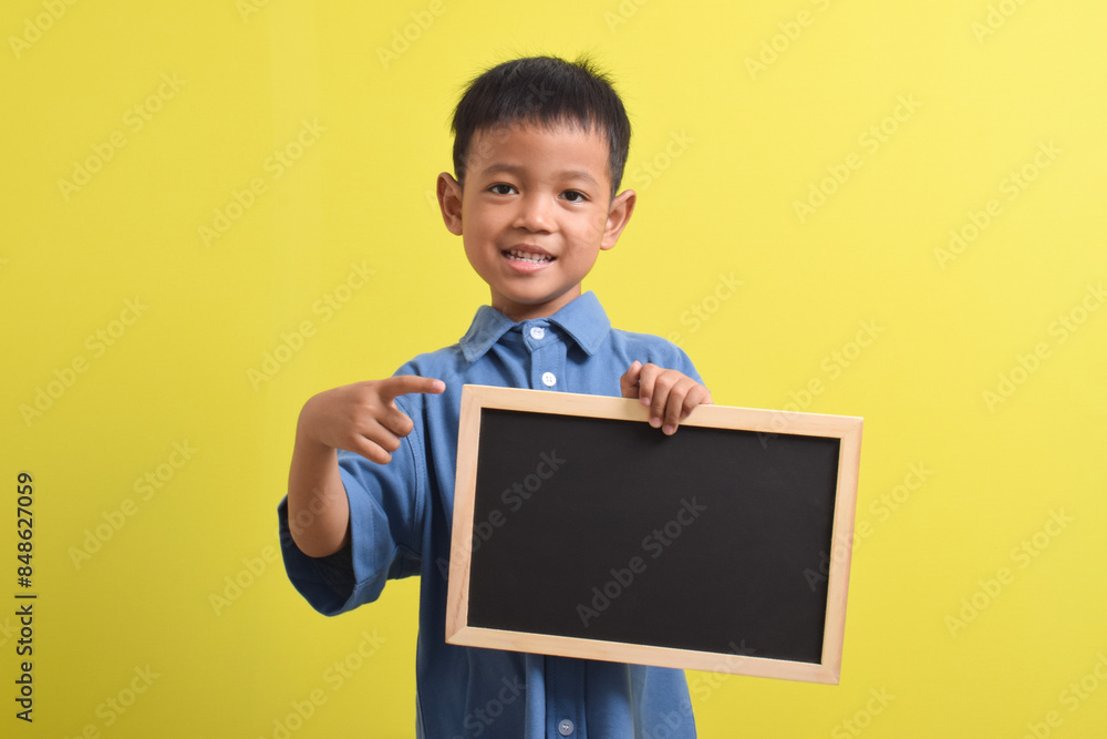 Cute little Asian boy holding a blank chalk board isolated on yellow background. Space for text, copy space, mockup banner Cute little Asian boy holding a blank chalk board isolated on yellow background. Space for text, copy space, mockup banner