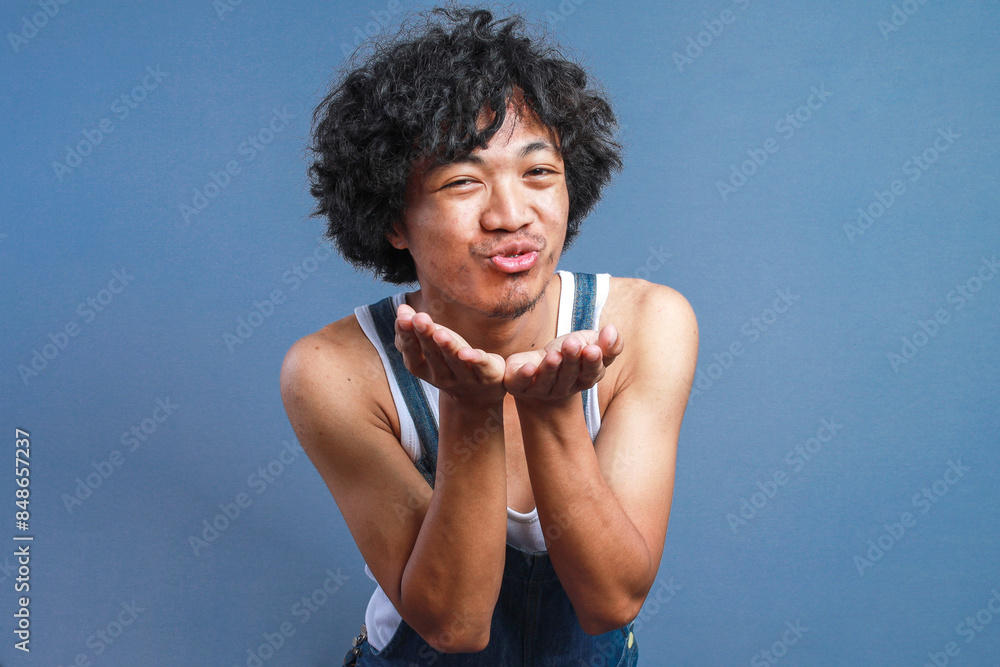 Young Curly Man Wearing Casual Dungarees and Sleeveless Shirt Blowing A Kiss With Hand On Air