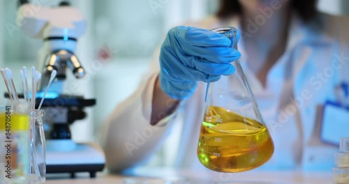 Technician stirs orange liquid in conical flask in lab photo