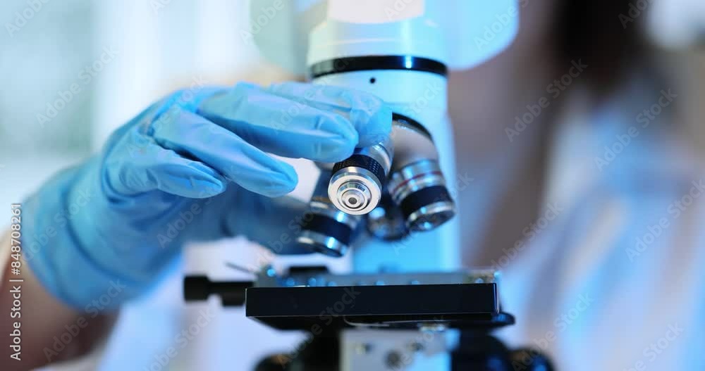 Technician turns microscope lenses using various enlargement Technician turns microscope lenses using various enlargement