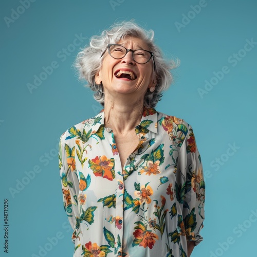 A beautiful elderly woman in an elegant shirt on an isolated blue background. The woman smiles and laughs. A place for the text.