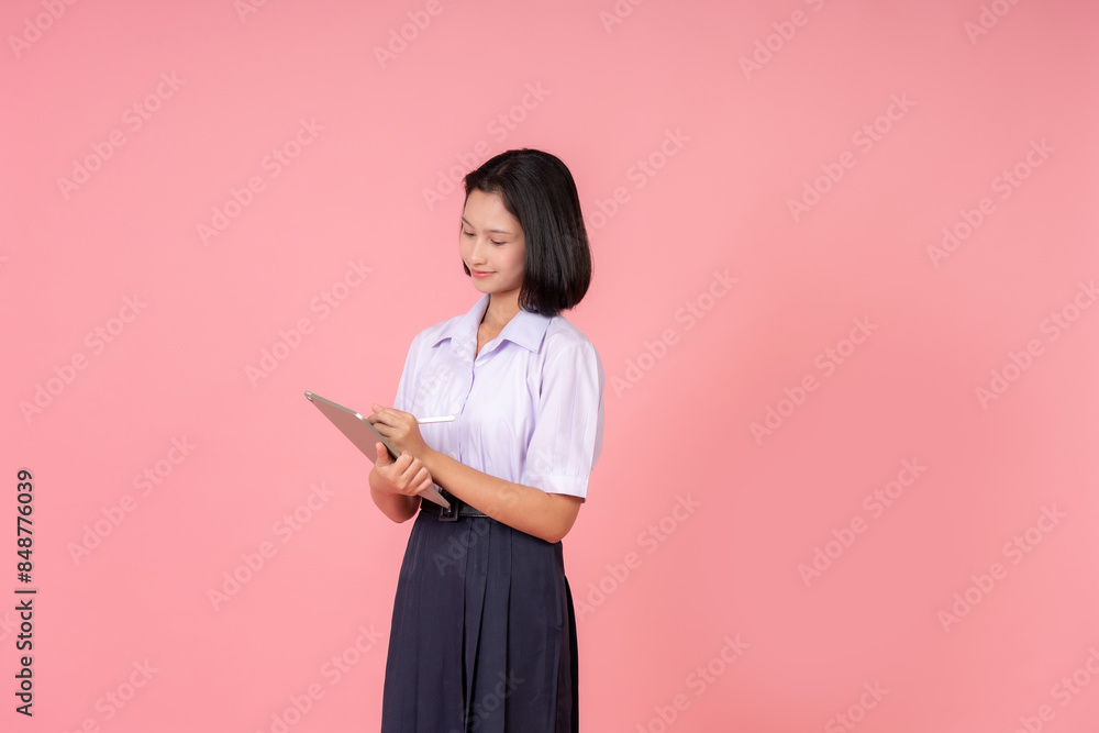 half body photo Asian female high school student holding a laptop sideways, making a report for the teacher about education and studying online, taking a photo in a studio with a pink background. half body photo Asian female high school student holding a laptop sideways, making a report for the teacher about education and studying online, taking a photo in a studio with a pink background.