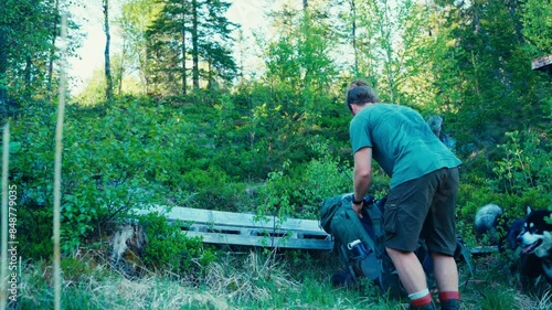 Backpacking Hiker With Alaskan Malamute Resting On The Wooden Bench Amidst Forest. Static Shot photo