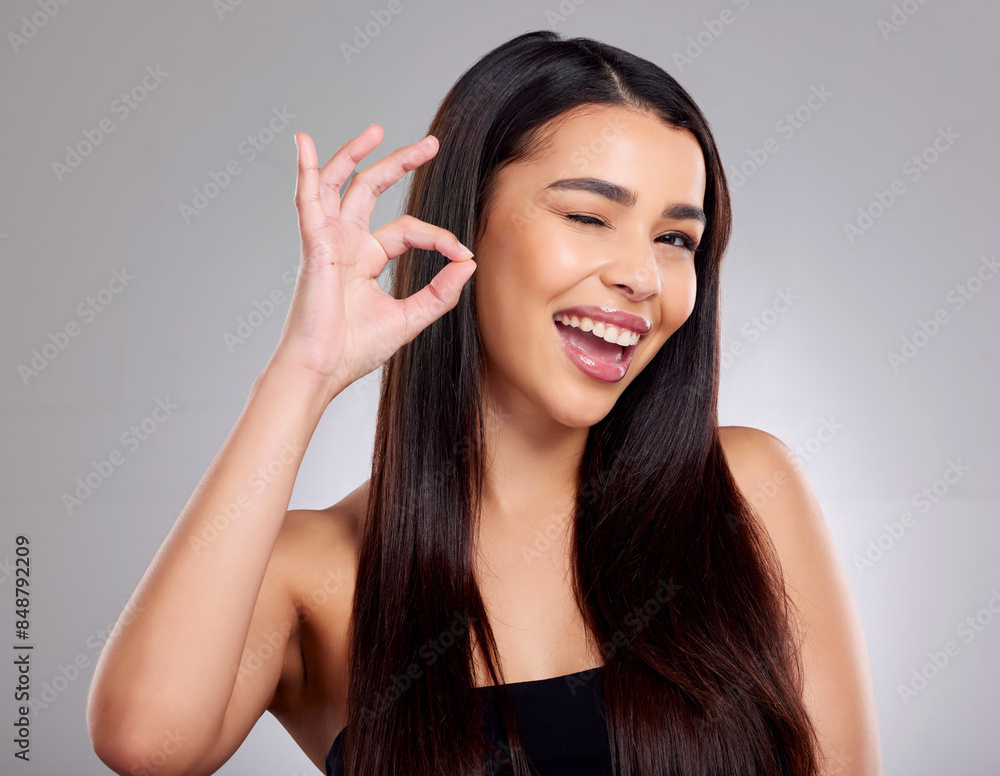 Portrait, woman and okay for hair in studio with satisfaction, keratin treatment and growth of product health. Smile, female person and wink or hand sign, collagen shine and beauty on grey background Portrait, woman and okay for hair in studio with satisfaction, keratin treatment and growth of product health. Smile, female person and wink or hand sign, collagen shine and beauty on grey background