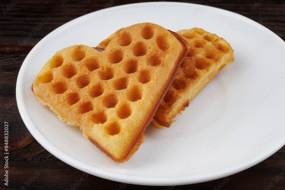 Two Viennese waffles lie on a white plate. Viennese waffles in the shape of a heart. Two Viennese waffles lie on a white plate. Viennese waffles in the shape of a heart.