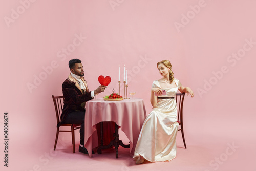 Regency Romance. Viscount and Viscountess sitting at table and having romantic dinner, celebrating marriage anniversary against pink background. History, retro and vintage, comparison of eras concept photo