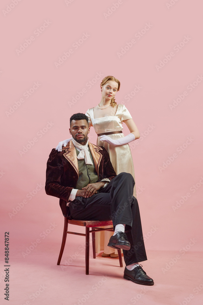 Classical noble portrait of regal gentleman in rich velvet coat, with lady standing confidently behind him against pink studio background. Concept of history, retro and vintage, comparison of eras Classical noble portrait of regal gentleman in rich velvet coat, with lady standing confidently behind him against pink studio background. Concept of history, retro and vintage, comparison of eras