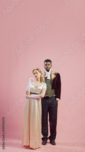 Victorian Confidence. Portrait of elegant young woman, princess standing handsome man, royal person against pink studio background. Concept of history, retro and vintage, comparison of eras photo