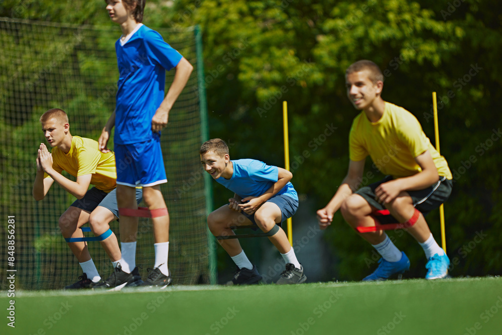 Obraz premium Groups of children toys training on outdoor football stadium doing squats with elastic bands. Athletic Training for Kids. Concept of sport, school, childhood, hobby, active lifestyle
