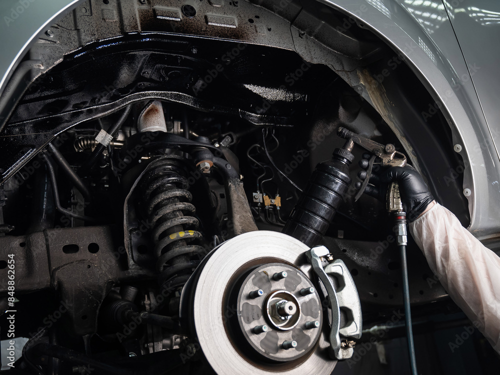 Fototapeta premium An auto mechanic applies anti-corrosion mastic to the underbody of a car.