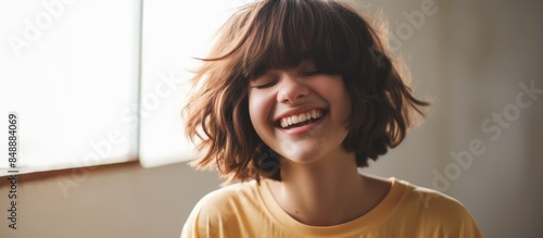 Close up shot of a joyful teenage girl with a bob haircut smiling genuinely with her eyes closed displaying her perfect teeth exuding positive human emotions in an indoor setting with copy space image photo