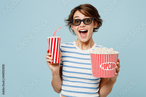 Fotografija Young happy woman wears striped t-shirt casual clothes 3d glasses watch movie film hold bucket of popcorn cup of soda pop in cinema isolated on plain pastel light blue cyan background studio portrait