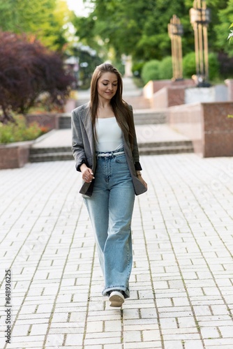 Pretty and attractive Caucasian young woman in stylish casual clothes posing with pleasure while walking in the park on a warm spring day. The concept of freedom, relax, style.