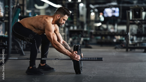 Athlete adding weight plates on his barbell, preparing for his weightlifting workout at gym, free space