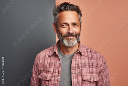 Portrait of a glad man in his 40s wearing a comfy flannel shirt while standing against solid pastel color wall