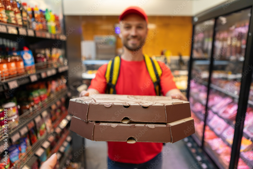 Fototapeta premium Delivery concept. Male pizza delivery courier holding cardboard boxes with freshly baked pizza, stretching it to camera