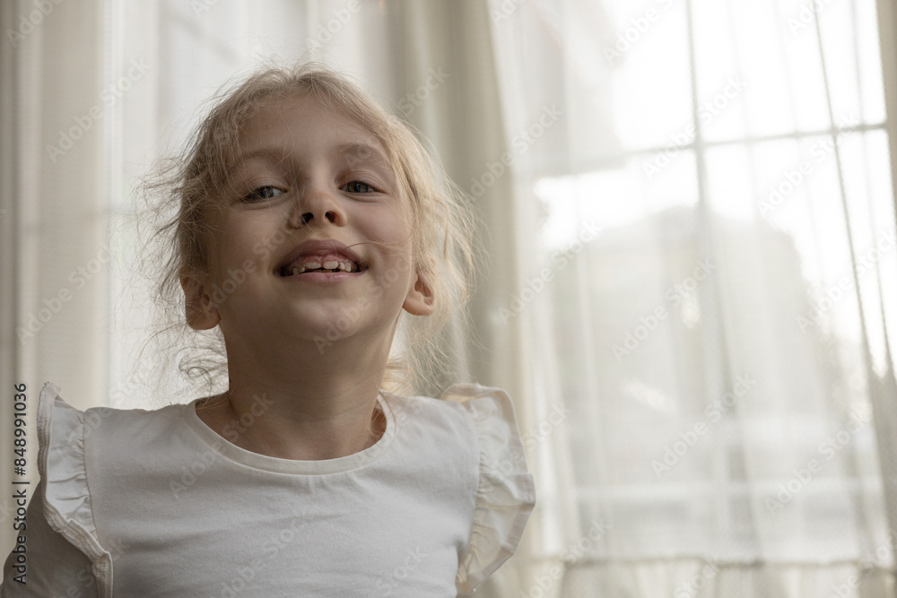 A child, little girl stands and laughs in the room in front of the window, close up. A child in a good mood, lifestyle concept, real person. Copy space A child, little girl stands and laughs in the room in front of the window, close up. A child in a good mood, lifestyle concept, real person. Copy space