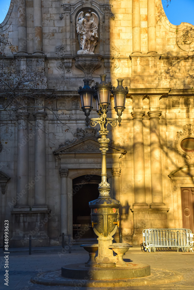 church facade in the city of barcelona with street lamp in the front, with the evening sunlight casting a shadow in the middle