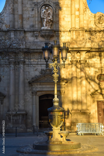 Obraz na płótnie church facade in the city of barcelona with street lamp in the front, with the evening sunlight casting a shadow in the middle w salonie