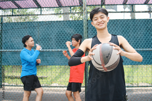 Young Man Holding A Ball While His Friends Drinks Water On The Background