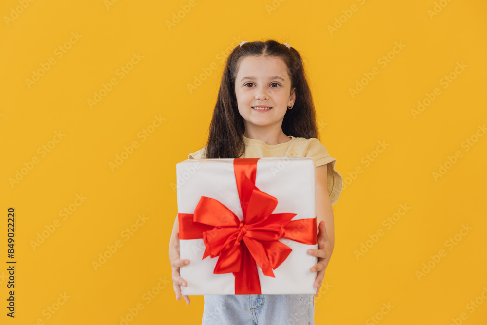 Excited smiling little girl holding gift box on yellow studio background with copy space Excited smiling little girl holding gift box on yellow studio background with copy space