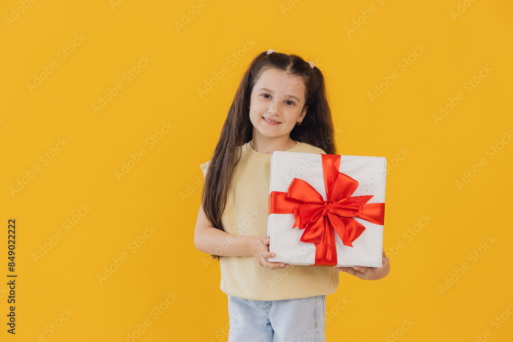 Excited smiling little girl holding gift box on yellow studio background with copy space Excited smiling little girl holding gift box on yellow studio background with copy space