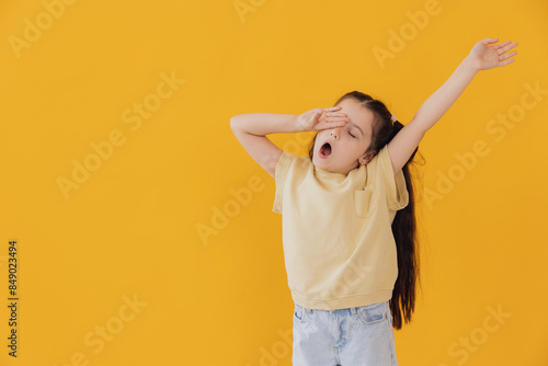 Canvas Print Sleepy little girl yawning on yellow studio background