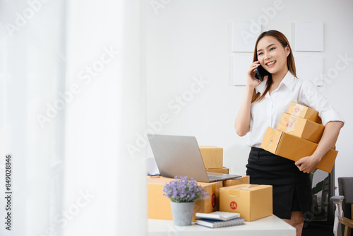 Owner SME Small and Medium Enterprises woman received orders from clients on phone and laptop then writing preparing products in parcel cardboard box packaging at home ready for delivery to customer