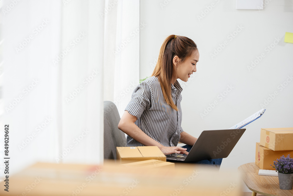 Owner SME Small and Medium Enterprises woman received orders from clients laptop then writing preparing products in parcel cardboard box packaging at home ready for delivery to customer Owner SME Small and Medium Enterprises woman received orders from clients laptop then writing preparing products in parcel cardboard box packaging at home ready for delivery to customer