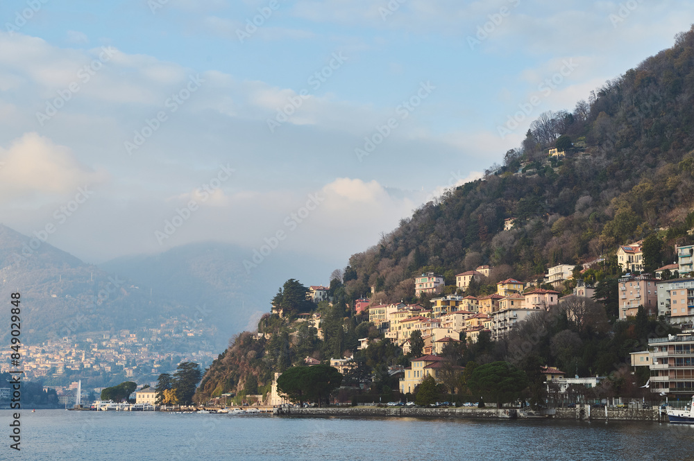 Scenic view of a lakeside village nestled among lush hills with serene waters and a cloudy sky Scenic view of a lakeside village nestled among lush hills with serene waters and a cloudy sky