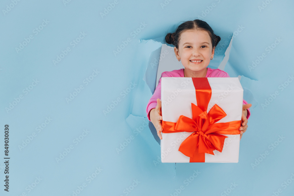 Adorable little girl peeking from ripped paper hole and holding gift. Valentines, Mother day, birthday or celebration concept. Adorable little girl peeking from ripped paper hole and holding gift. Valentines, Mother day, birthday or celebration concept.