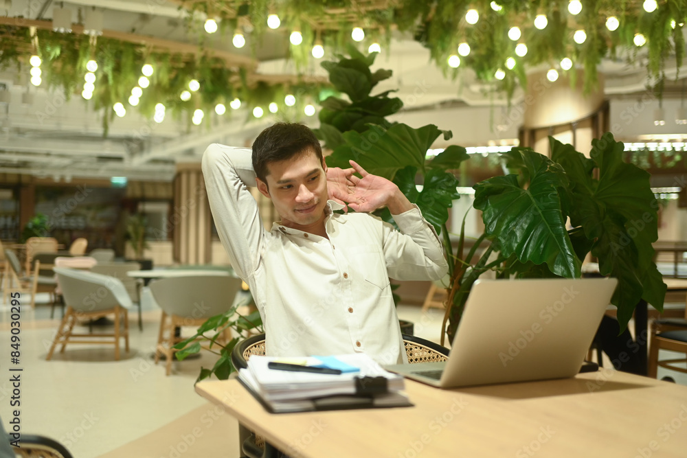 Smiling asian businessman taking a break from computer work relaxing at table in office lounge Smiling asian businessman taking a break from computer work relaxing at table in office lounge