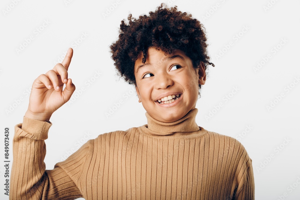 A spirited young african american girl joyfully pointing upwards, excited and full of energy against a clean white background A spirited young african american girl joyfully pointing upwards, excited and full of energy against a clean white background