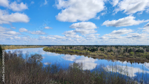 Panoramic view of river bend, forest and blue sky. Beautiful reflection of white clouds in water at sunny day. Aerial view of picturesque background. High quality photo