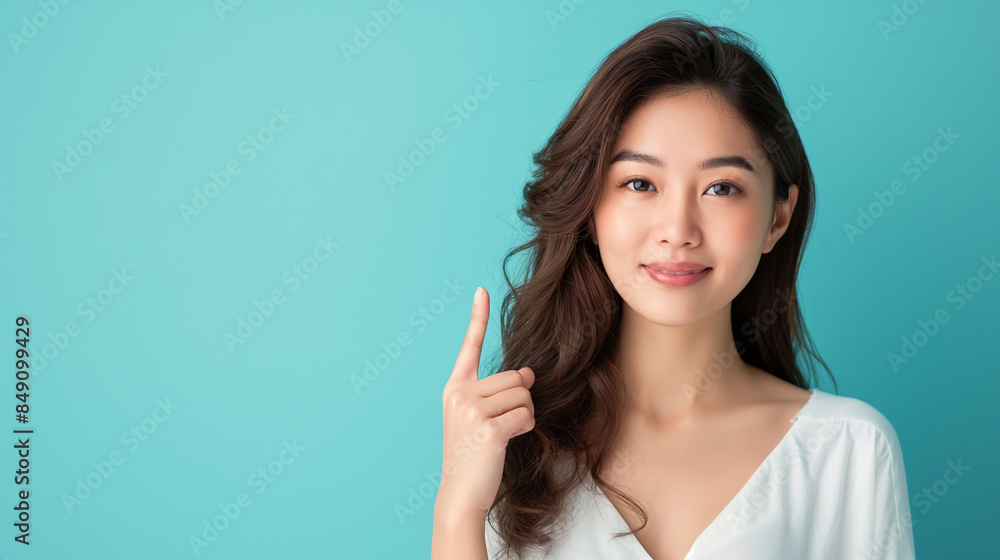 An elegant Asian woman presenting with confidence, pointing towards a copy space light blue background, highlighting her beauty and grace. An elegant Asian woman presenting with confidence, pointing towards a copy space light blue background, highlighting her beauty and grace.
