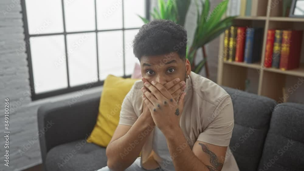 Gobsmacked african american guy covering mouth with hands on living room sofa - shocking secret prompts horrified home mistake Gobsmacked african american guy covering mouth with hands on living room sofa - shocking secret prompts horrified home mistake